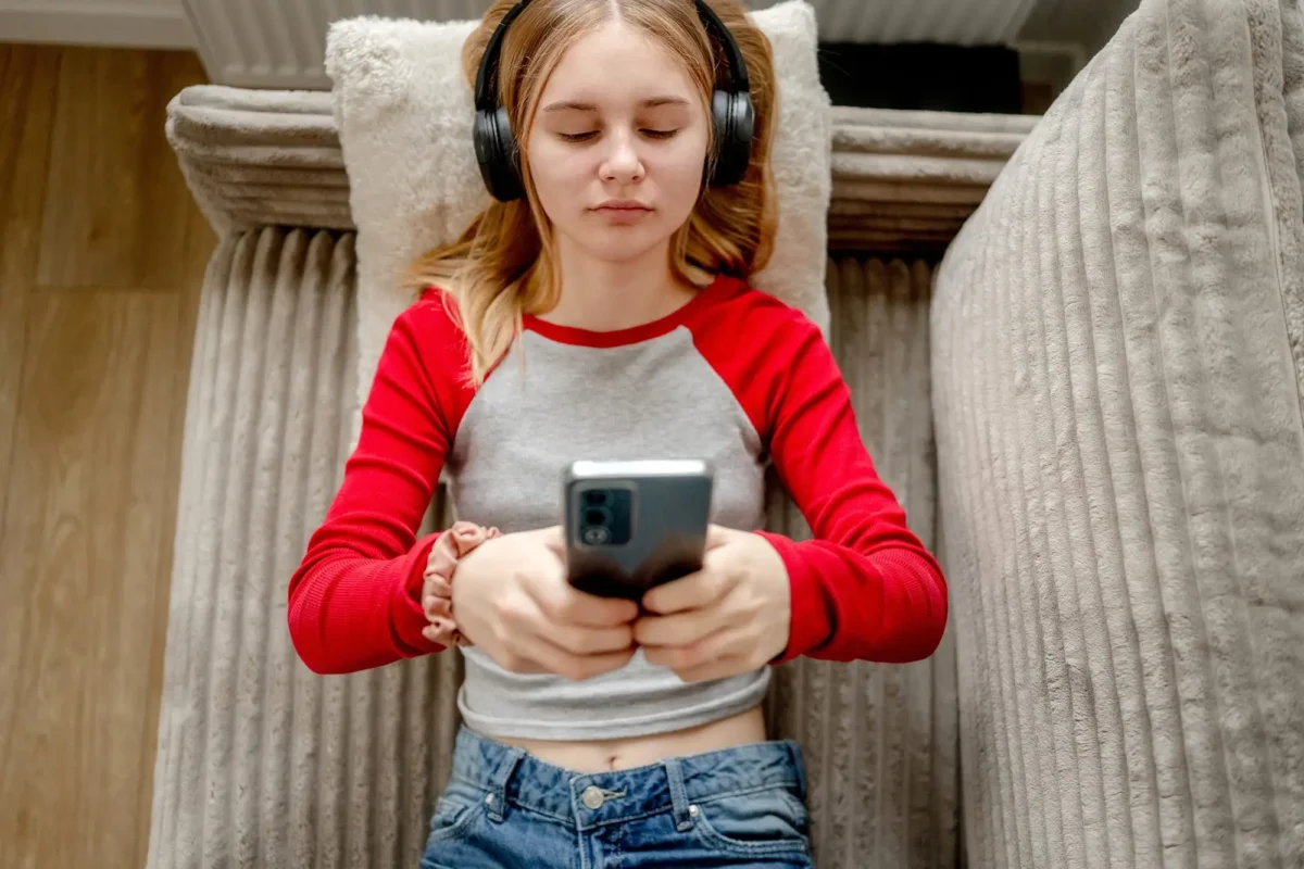 shutterstock_2720531135 1 | TVGURU.cz žena se sluchátky a mobilem leží na gauči