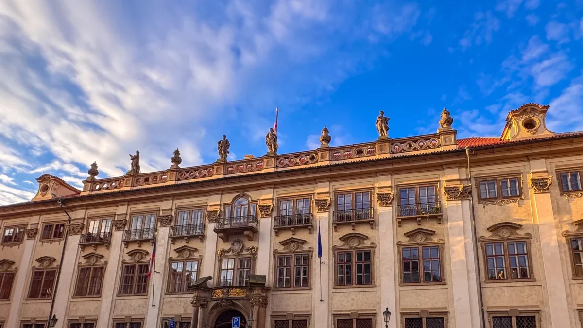 Historic stone building with ornate statues along the roofline beneath a bright blue sky with wispy clouds.