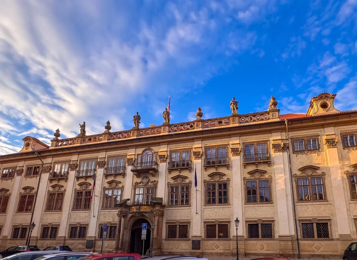Historic stone building with ornate statues along the roofline beneath a bright blue sky with wispy clouds.