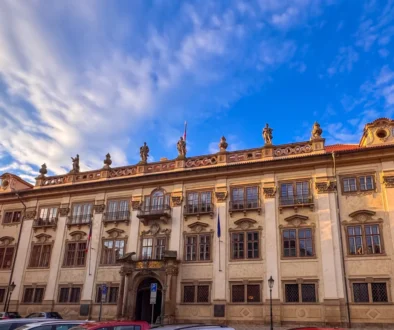 Historic stone building with ornate statues along the roofline beneath a bright blue sky with wispy clouds.