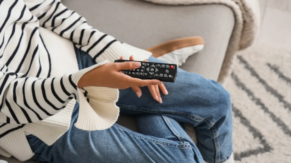 Žena sedí na gauči a v ruce drží TV ovladač.