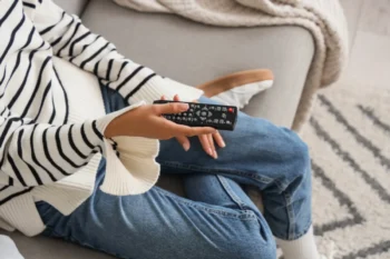 Žena sedí na gauči a v ruce drží TV ovladač.