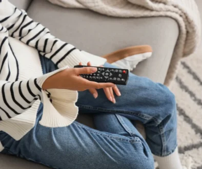 Žena sedí na gauči a v ruce drží TV ovladač.
