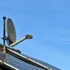 Satellite dish mounted on a pitched roof beside solar panels against a clear blue sky.