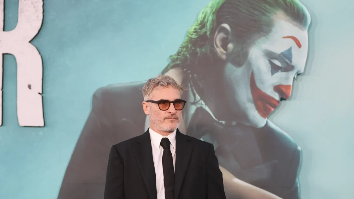 Joaquin Phoenix stojí před reklamou na Jokera.