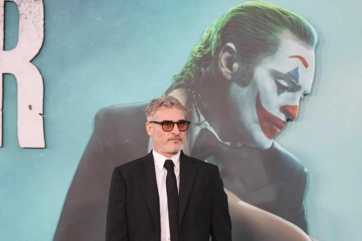 Joaquin Phoenix stojí před reklamou na Jokera.