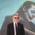 Joaquin Phoenix stojí před reklamou na Jokera.
