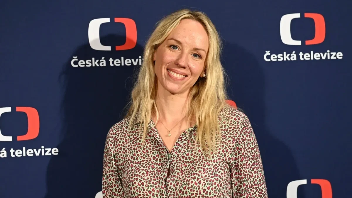 Petra Hřebíčková stojí před nápisy Česká televize a usmívá se.