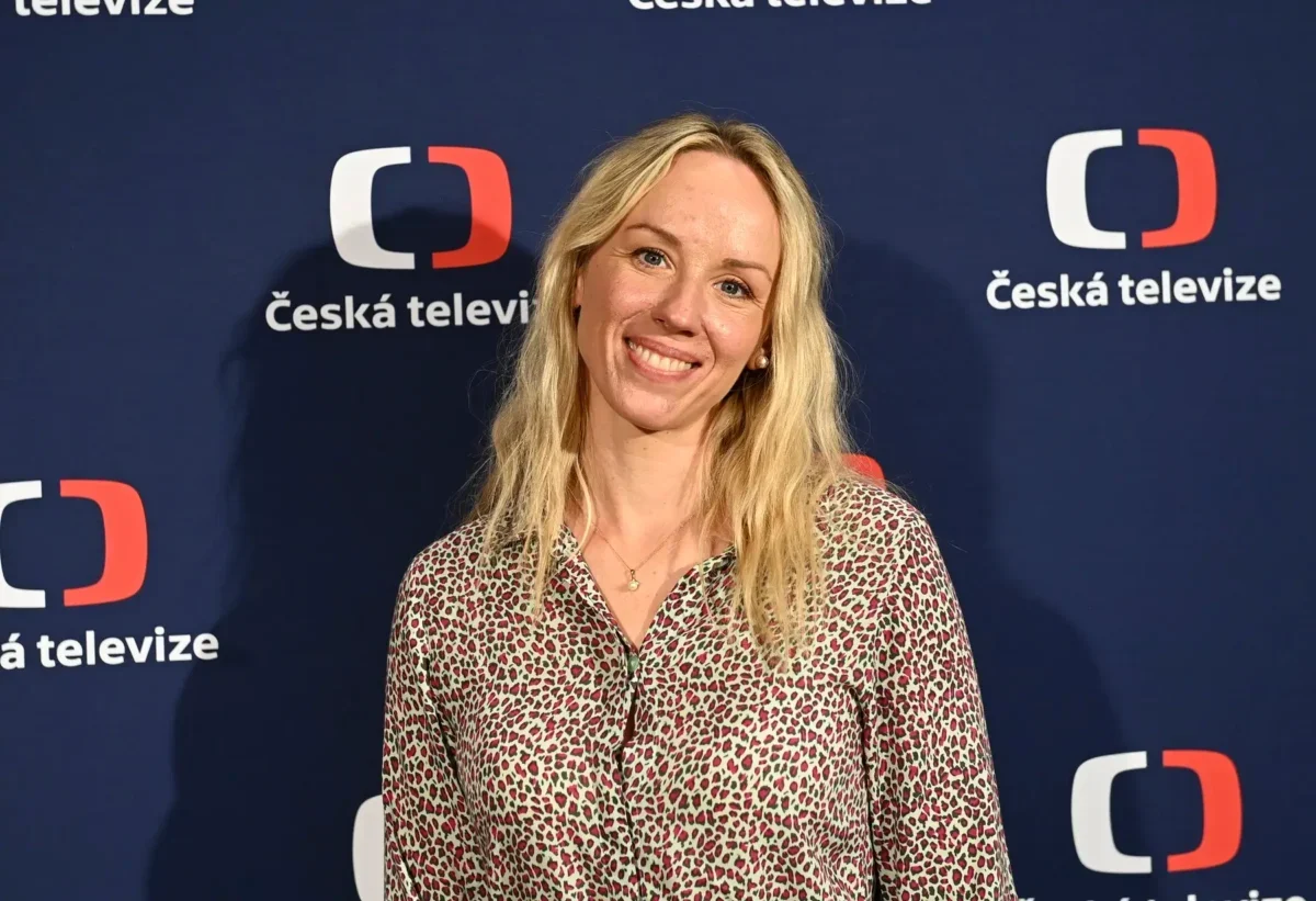 Petra Hřebíčková stojí před nápisy Česká televize a usmívá se.